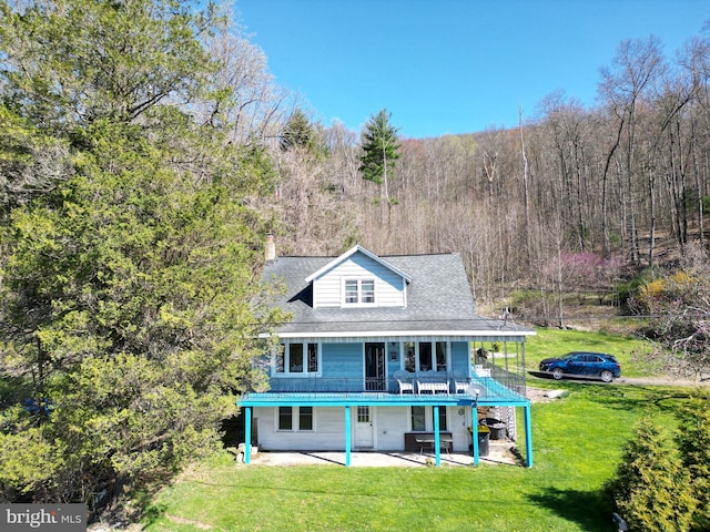 rear view of house featuring a chimney, a lawn, a patio area, and a view of trees