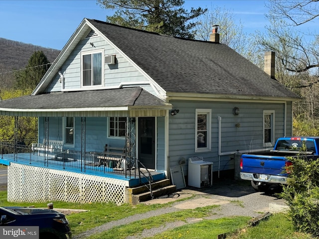 back of property with covered porch, a shingled roof, and a chimney