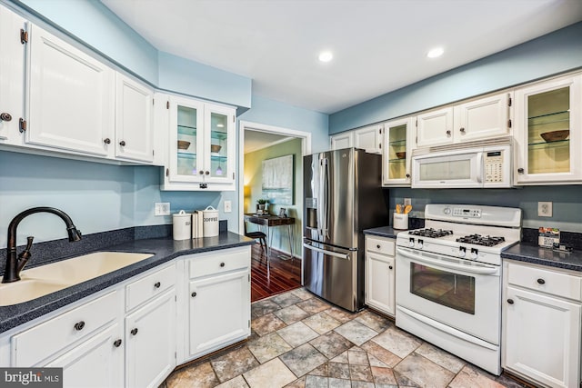 kitchen with dark countertops, recessed lighting, white cabinets, a sink, and white appliances