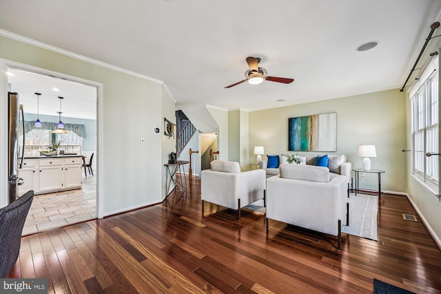 living area featuring ceiling fan, hardwood / wood-style flooring, baseboards, stairway, and crown molding