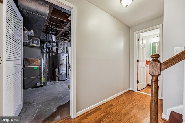 hallway with baseboards, water heater, heating unit, and wood finished floors