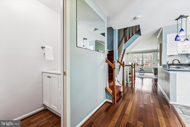 corridor featuring dark wood-style floors, baseboards, stairway, and a sink