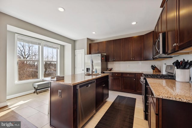 kitchen featuring an island with sink, appliances with stainless steel finishes, decorative backsplash, and light stone counters