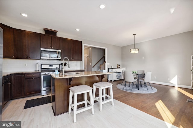 kitchen with stainless steel appliances, a sink, an island with sink, light stone countertops, and a kitchen breakfast bar