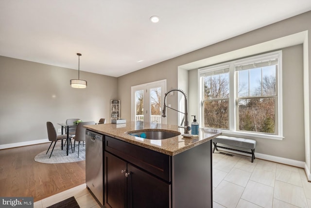 kitchen featuring baseboards, a sink, light stone countertops, hanging light fixtures, and stainless steel dishwasher