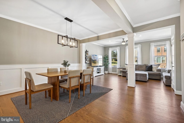 dining room featuring wainscoting, wood finished floors, crown molding, ornate columns, and a decorative wall