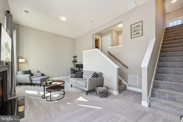 living room featuring carpet floors, visible vents, stairway, a lit fireplace, and baseboards