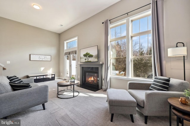 living area featuring a fireplace with flush hearth, carpet flooring, visible vents, and a high ceiling