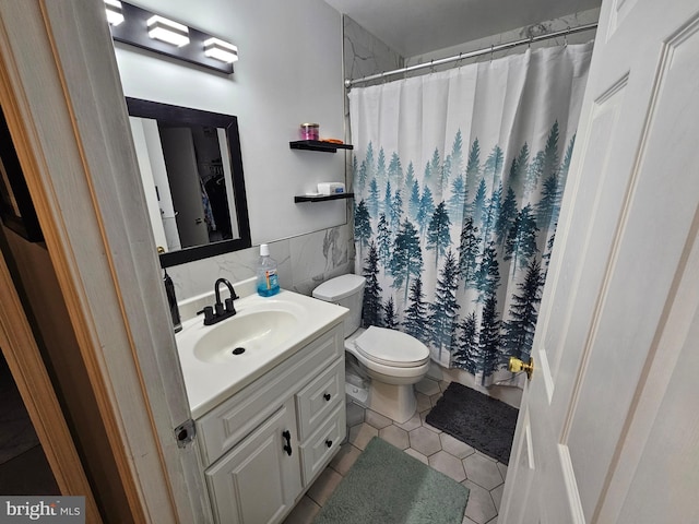 bathroom with toilet, a wainscoted wall, tile patterned floors, vanity, and tile walls