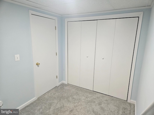 unfurnished bedroom with baseboards, a closet, a drop ceiling, and light colored carpet