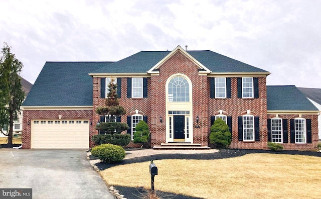 colonial-style house featuring driveway, an attached garage, a shingled roof, and brick siding