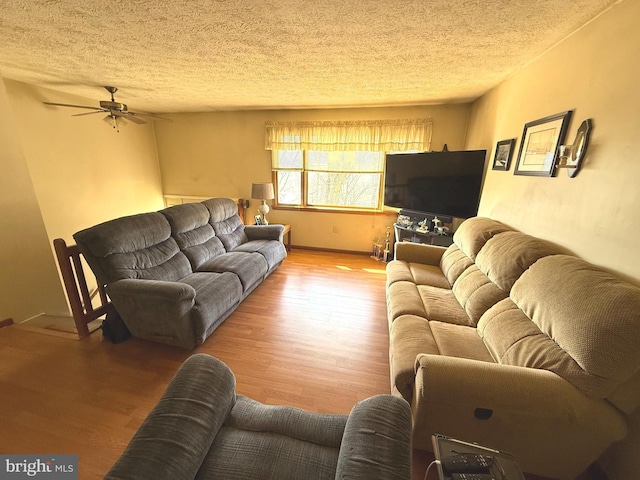 living area with ceiling fan, a textured ceiling, baseboards, and wood finished floors