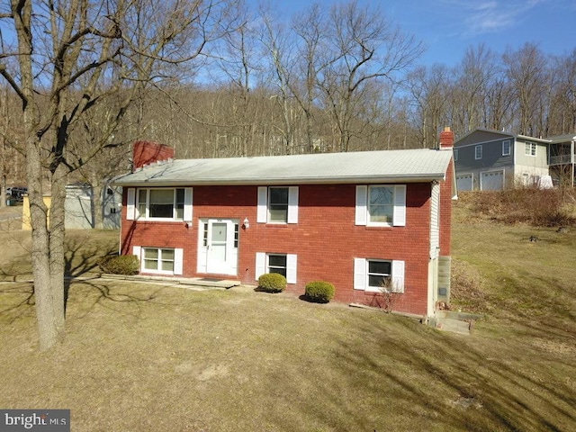 raised ranch with brick siding, a chimney, and a front lawn