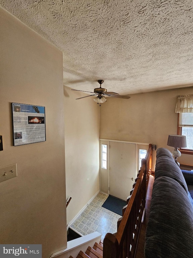 foyer entrance with a ceiling fan, a textured ceiling, and baseboards