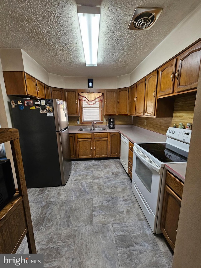 kitchen featuring white appliances, a sink, visible vents, light countertops, and brown cabinets