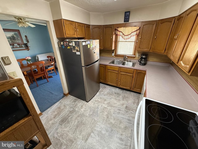 kitchen featuring range with electric cooktop, brown cabinetry, a sink, and freestanding refrigerator