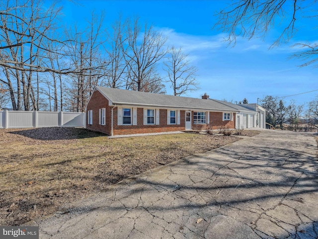 view of front of house featuring driveway, a chimney, fence, a front lawn, and brick siding