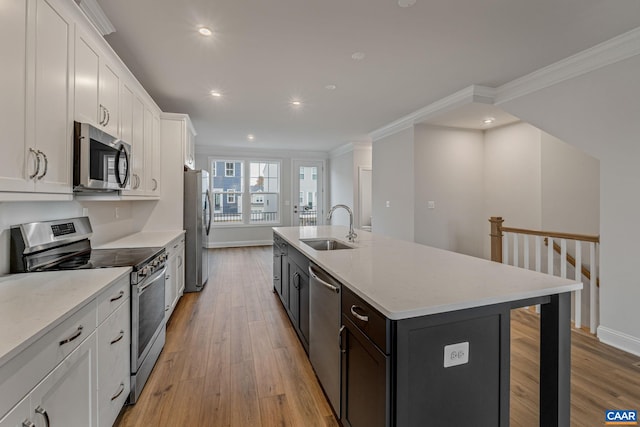 kitchen with light stone counters, a kitchen island with sink, stainless steel appliances, a sink, and white cabinetry