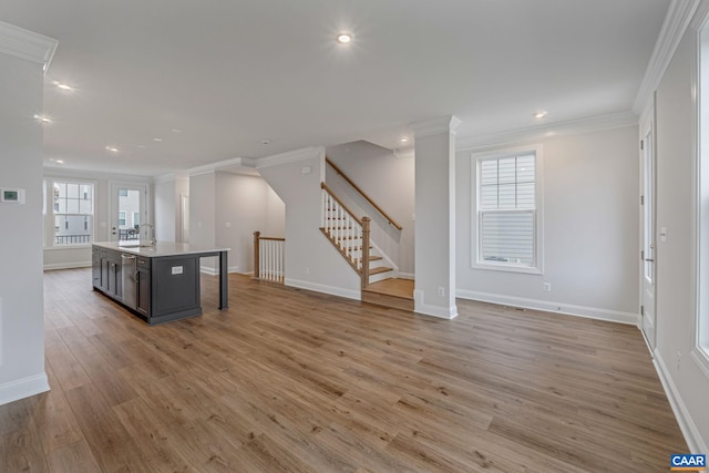 kitchen featuring a kitchen breakfast bar, open floor plan, light wood-style floors, an island with sink, and crown molding