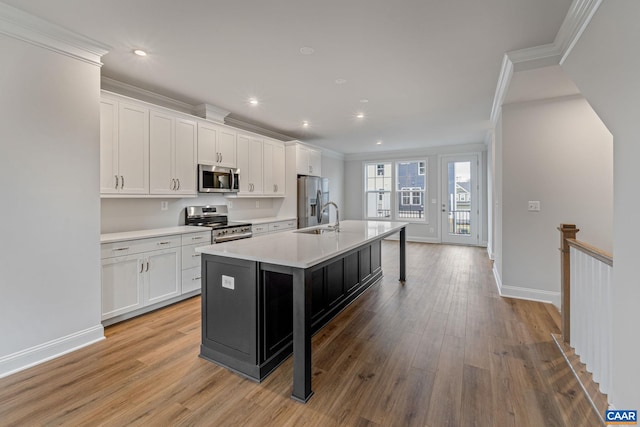 kitchen featuring stainless steel appliances, light countertops, ornamental molding, white cabinets, and an island with sink