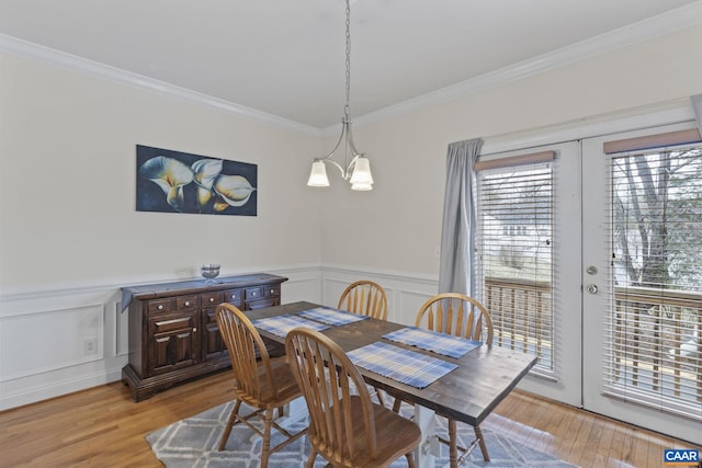 dining room with french doors, a wainscoted wall, crown molding, an inviting chandelier, and light wood-style floors