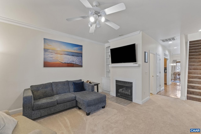 living room featuring visible vents, light colored carpet, a fireplace with flush hearth, ornamental molding, and stairs