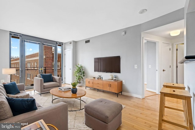 living room featuring floor to ceiling windows, light wood finished floors, visible vents, and baseboards