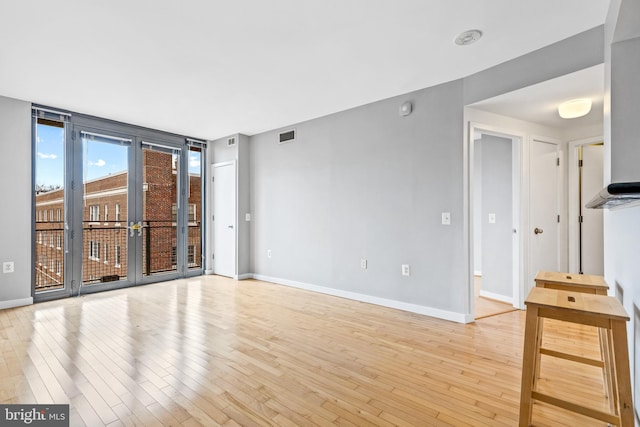 unfurnished living room featuring light wood-style floors, visible vents, expansive windows, and baseboards