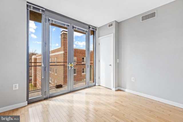 unfurnished room featuring expansive windows, wood finished floors, visible vents, and baseboards