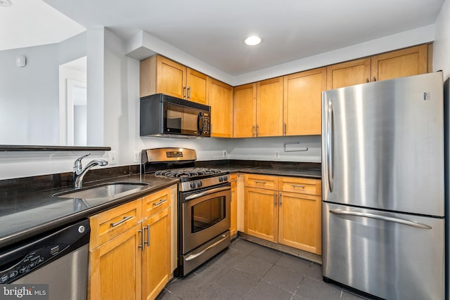 kitchen with dark tile patterned floors, a sink, appliances with stainless steel finishes, brown cabinets, and dark stone counters