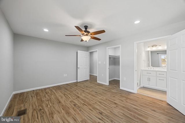 unfurnished bedroom with connected bathroom, visible vents, baseboards, light wood-type flooring, and a walk in closet