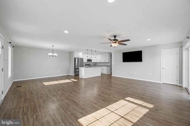 unfurnished living room featuring ceiling fan with notable chandelier, dark wood-type flooring, baseboards, and recessed lighting