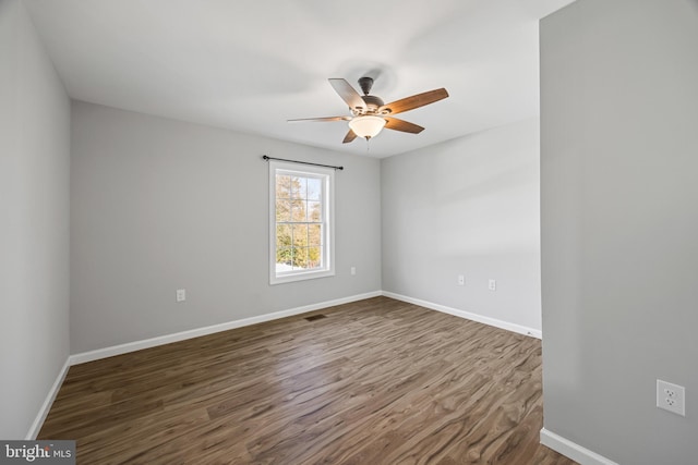 empty room featuring a ceiling fan, visible vents, dark wood finished floors, and baseboards