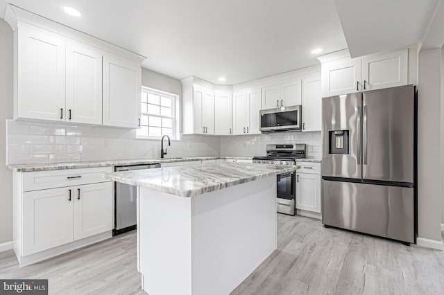 kitchen with white cabinets, light wood-style flooring, a kitchen island, appliances with stainless steel finishes, and light stone counters