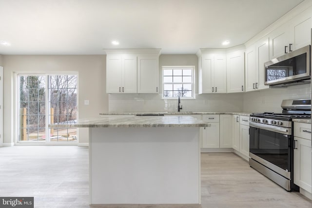 kitchen featuring decorative backsplash, appliances with stainless steel finishes, a center island, light stone countertops, and white cabinetry