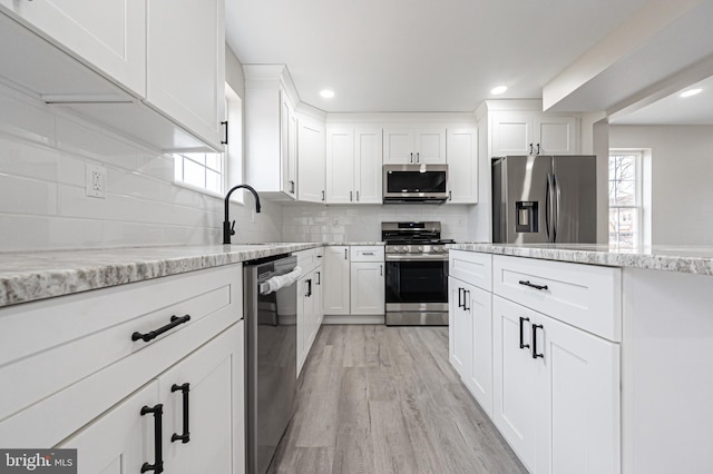 kitchen with stainless steel appliances, backsplash, light wood-style floors, white cabinets, and light stone countertops