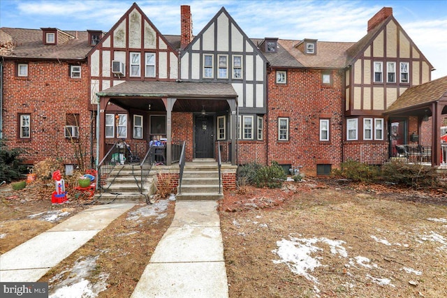 english style home featuring brick siding, a chimney, stucco siding, a shingled roof, and covered porch