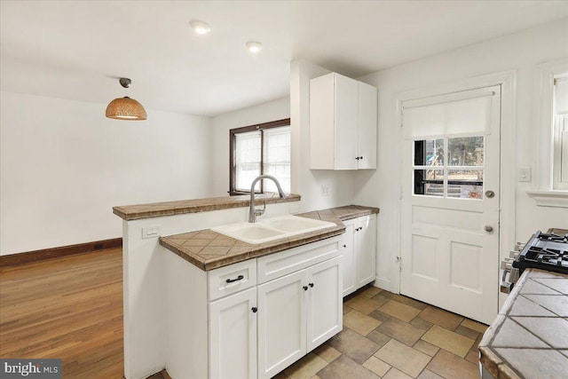 kitchen featuring a peninsula, a sink, white cabinets, hanging light fixtures, and stainless steel range