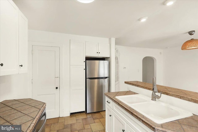 kitchen featuring tile countertops, freestanding refrigerator, stone finish flooring, white cabinets, and a sink