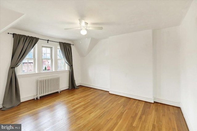 bonus room with baseboards, a ceiling fan, radiator, vaulted ceiling, and light wood-type flooring