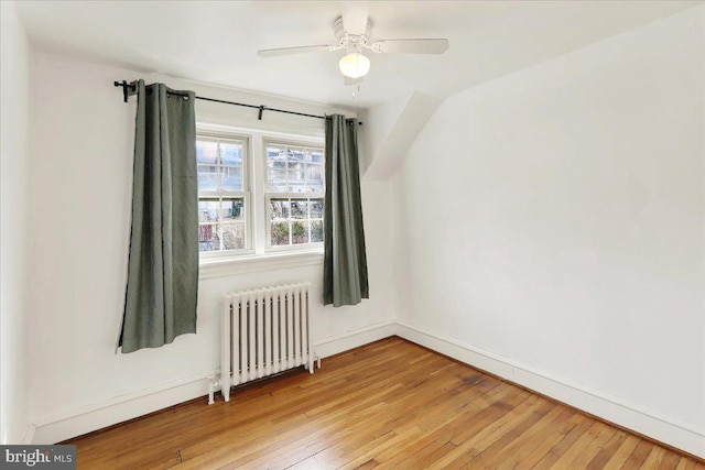 empty room with light wood-style floors, baseboards, radiator heating unit, and a ceiling fan