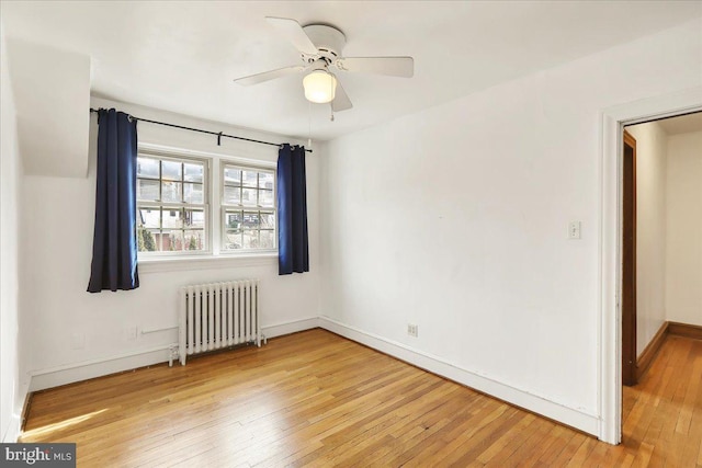 spare room featuring ceiling fan, radiator heating unit, light wood-type flooring, and baseboards