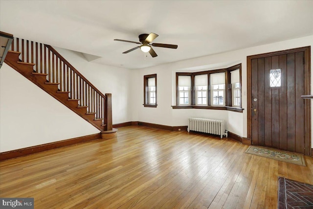 entryway with light wood finished floors, baseboards, radiator, ceiling fan, and stairs