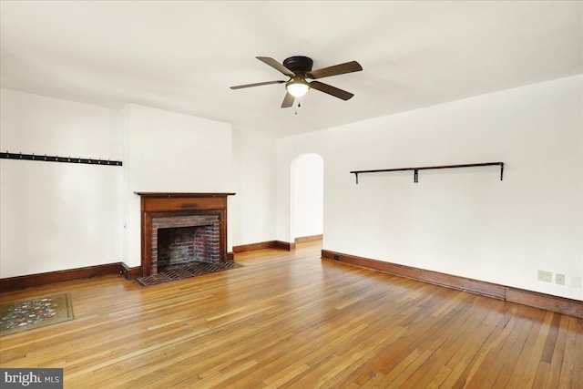 unfurnished living room with arched walkways, baseboards, light wood-style flooring, ceiling fan, and a fireplace