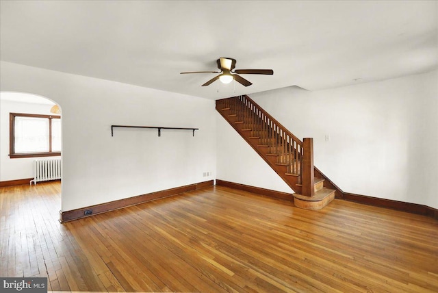 unfurnished living room with ceiling fan, wood finished floors, baseboards, stairs, and radiator