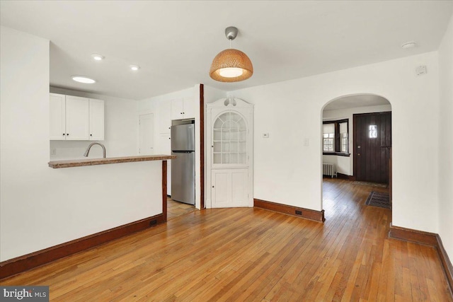 unfurnished living room featuring arched walkways, baseboards, light wood finished floors, and radiator heating unit