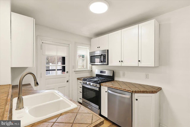 kitchen with stainless steel appliances, tile counters, white cabinets, and a sink