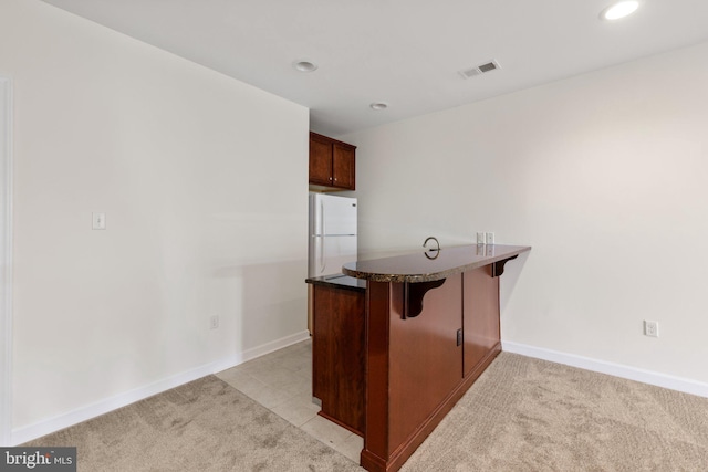 kitchen featuring dark countertops, light colored carpet, visible vents, freestanding refrigerator, and a peninsula