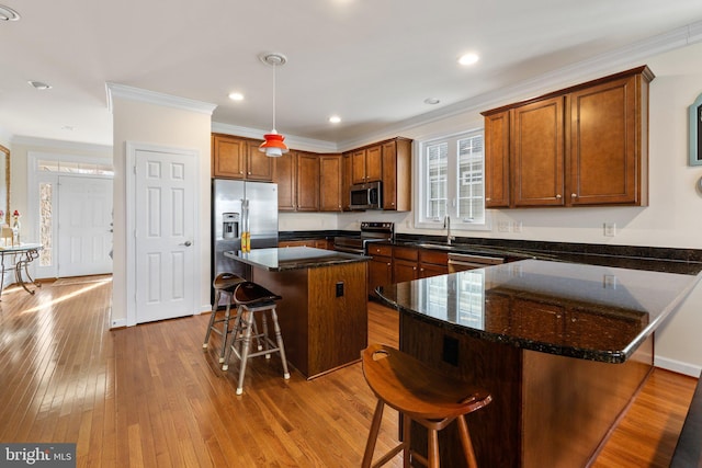 kitchen featuring a center island, appliances with stainless steel finishes, dark stone countertops, light wood-type flooring, and a kitchen breakfast bar