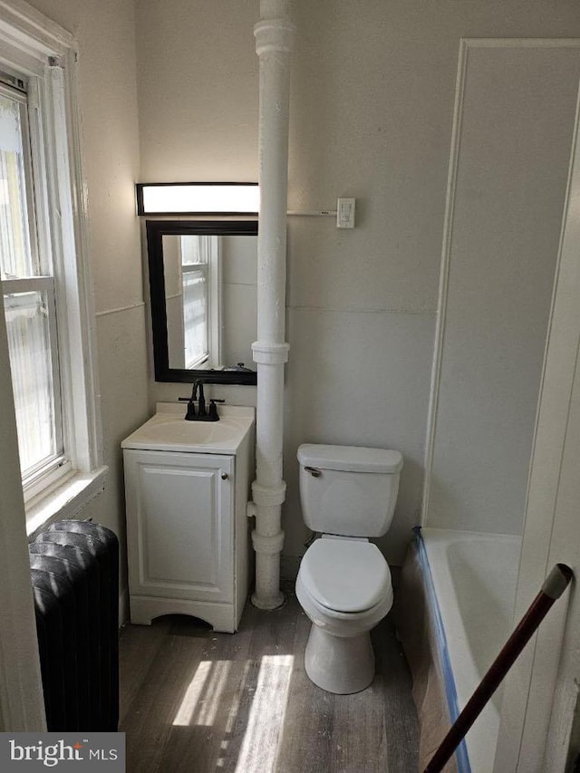 bathroom with toilet, a washtub, wood finished floors, and vanity